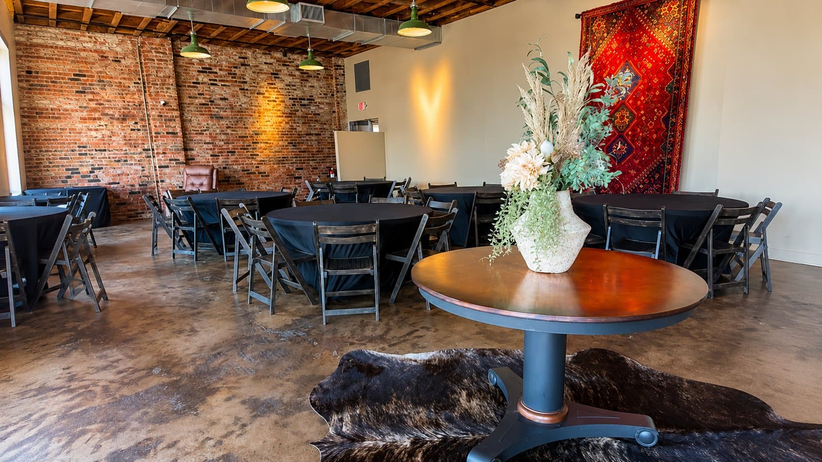 Round tables set with black linens near a woven vase centerpiece and a red woven wall hanging